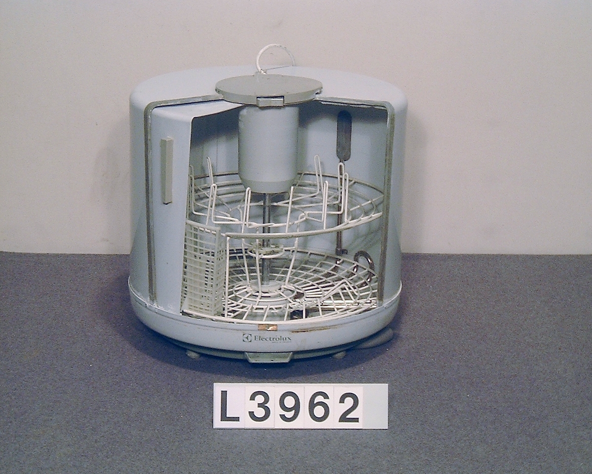 Electrolux  bänkdiskmaskinen  D10c "runda burken". Cylindrisk bänkdiskmaskin med skjutlucka och hela apparaten är lackerad i grå- vitt med grå gummi lister. Gummilisterna är torra, midjelisten är borta och påtappningsslangen är ej original.