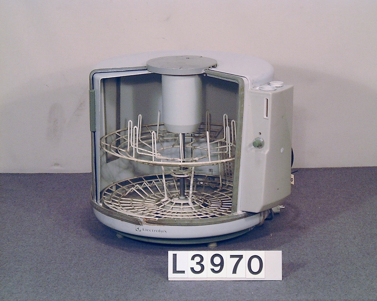 Electrolux helautomatiska variant av bänkdiskmaskinen "runda burken". Cylindrisk bänkdiskmaskin med skjutlucka. Hela apparaten är lackerad i grå- vitt med grå gummilister. Gummilisterna är torra.