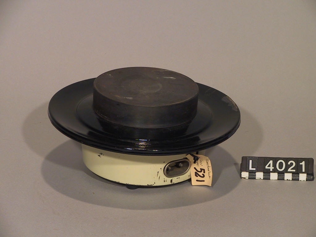 Liten spisplatta utan effektreglage. Spillkragen är i svart emalj och höljet målat i bengult. Plattan står på fyra gummifötter. Troligen är den inte använd. Plattan kopplas med en våffeljärnssladd.