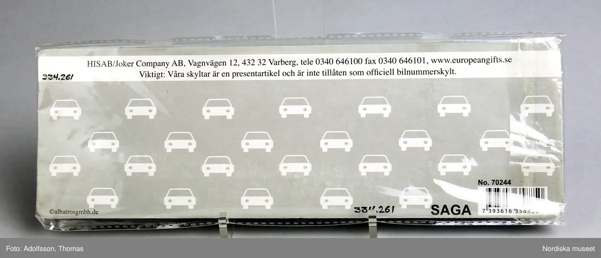 Namnskylt av plåt, avsedd för barnvagn i originalförpackning. Är utformad som en registreringsskylt för bil. Rektangulär, vit med svart ram. På skylten finns namnet Saga samt en svensk flagga och nationsbokstaven S. I övre hörnen hål.

/ C Hammarlund-Larsson 2019-01-25