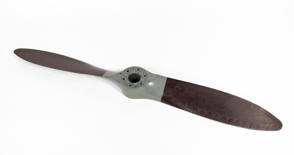 Tvåbladig träpropeller till SK 12. Propellern är målad grå och har skoning på bladen. Baksidan av propellerbladen är bruna. 
Propellern ligger i en trälåda. På locket står det att den tillhör SK 12/70.