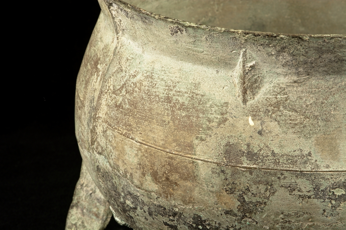 Trefotsgryta av brons. Signerad av tillverkaren i form av att upphöjt bomärke i metallen. Grytan har även en omsorgsfullt utförd lagning.

 Mynningen på grytan har en diameter på ca 25cm.