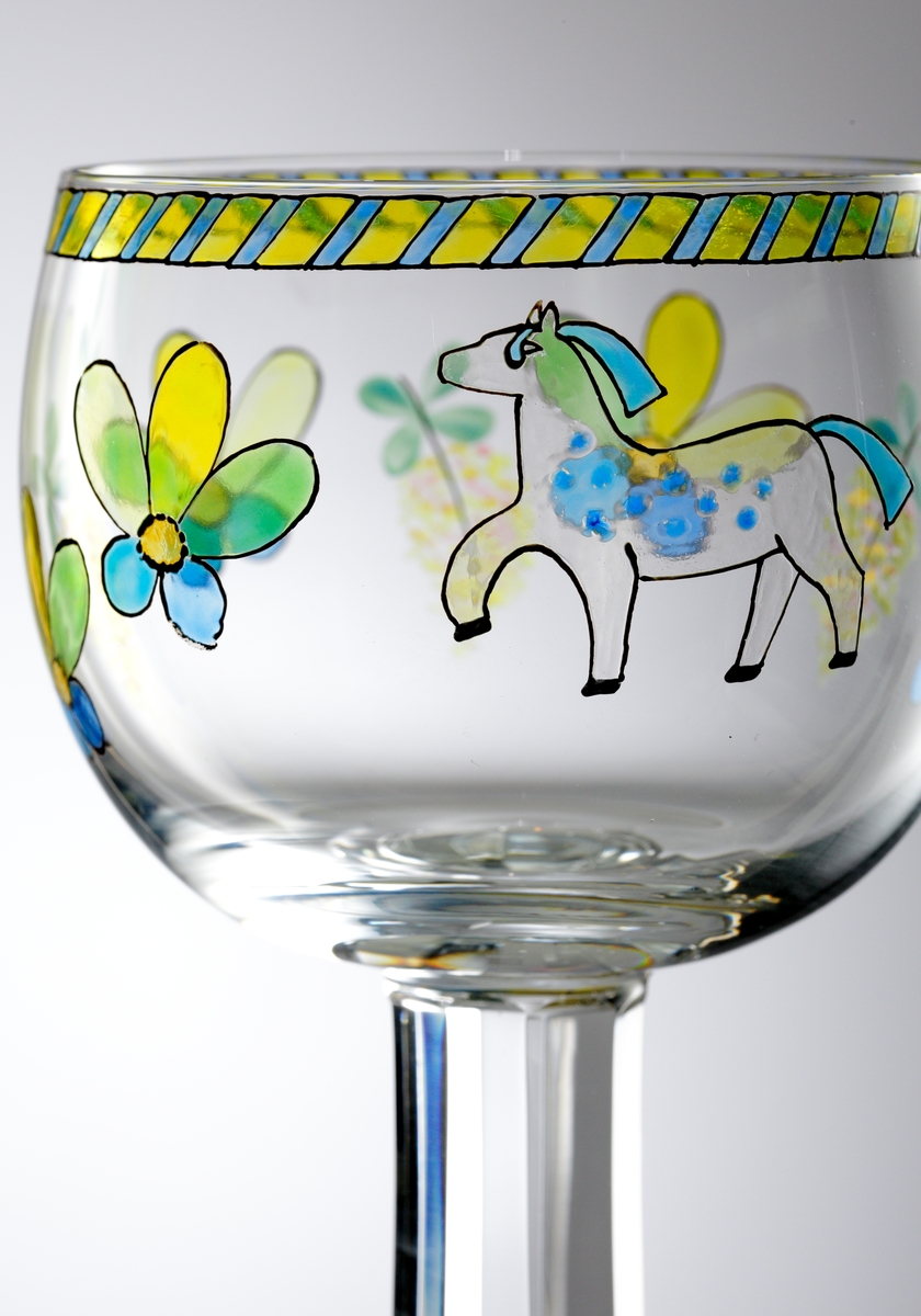 Vinglas av Gunnar Cyrén med generös kupa bemålad med "sverigemotiv" i form av människor och blommor i företrädelsevis blått och gult.
Facettslipat ben.