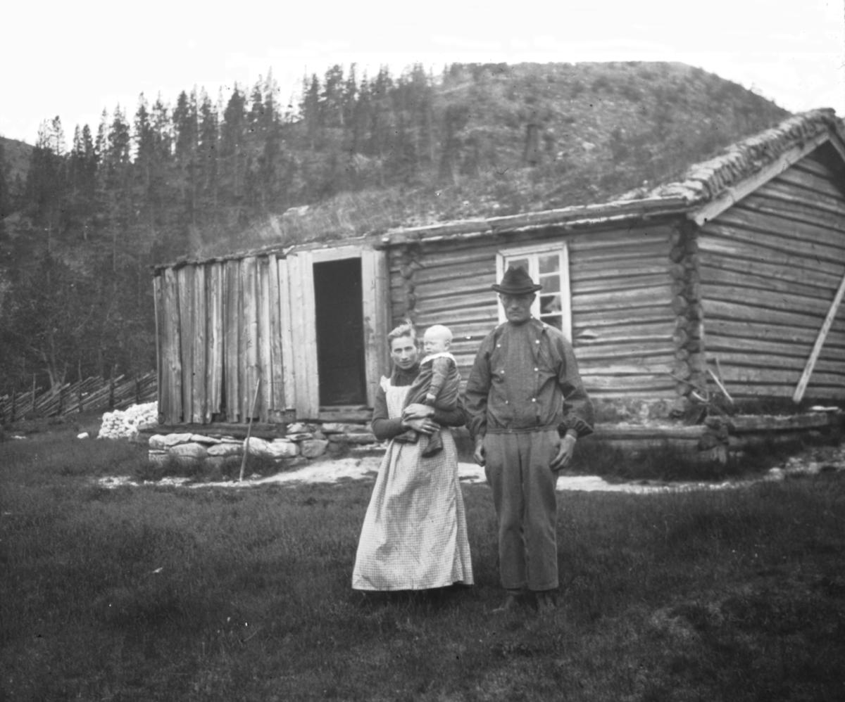 Et par, mann og kvinne med lite barn på armen, utenfor bygning. Antatt Valdres.