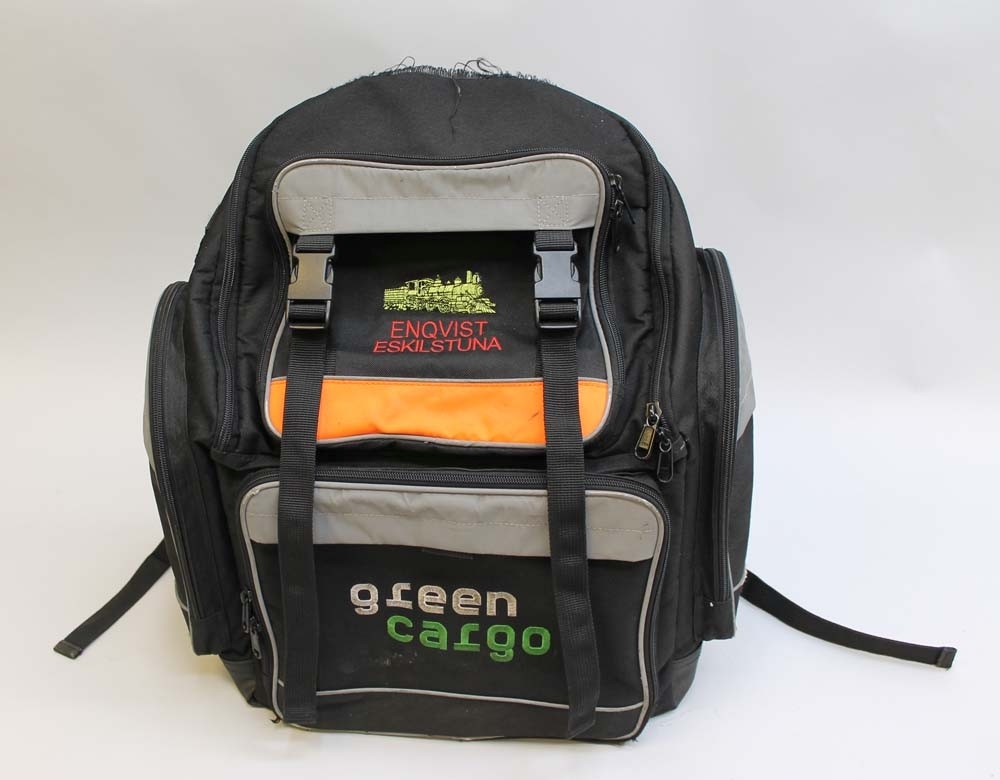 Svart ryggsäck med reflexer och ett fält med orange varseltextil. På framsidan är det broderat ett gult ånglok och "GÖRAN ENQVIST ESKILSTUNA" i rött samt "green cargo" i vitt och grönt. Ryggsäcken har två sidofack på vardera sida och fyra fack framtill samt diverse mindre fack inuti de två större främre facken såsom hållare för pennor, mobiltelefon, kort och dylikt. Huvudfacket har en vadderad avskiljare för t.ex. en laptop.