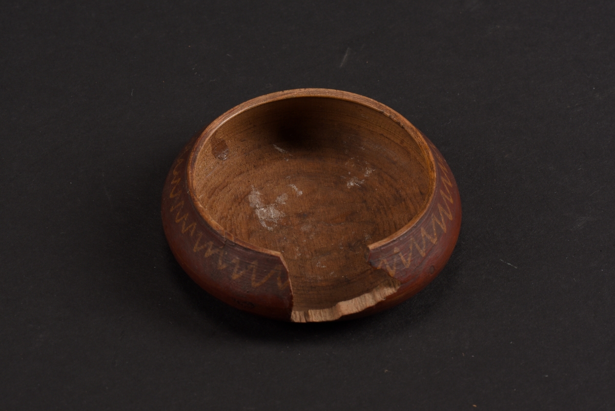 Rund, svarvad, ask med lock tillverkad av bok. Asken är målad på utsidan i rött med gula mönster; runt asken ett sicksackmönster och på locket ett årtal, 1760, samt en stiliserad lilja. Asken är skadad och en bit saknas.