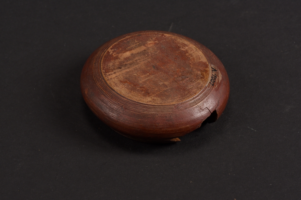 Rund, svarvad, ask med lock tillverkad av bok. Asken är målad på utsidan i rött med gula mönster; runt asken ett sicksackmönster och på locket ett årtal, 1760, samt en stiliserad lilja. Asken är skadad och en bit saknas.