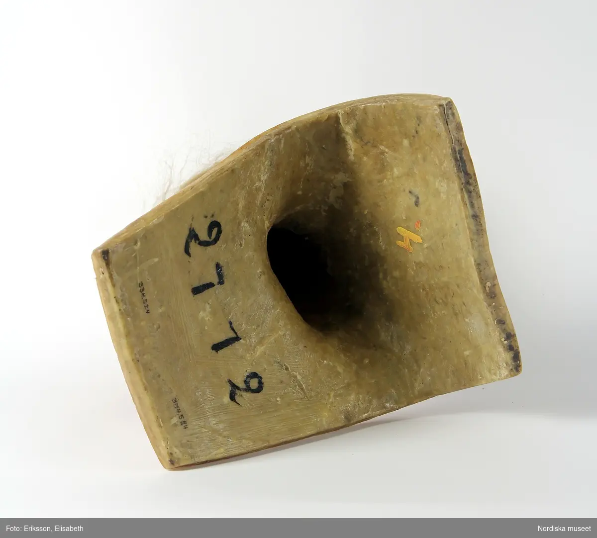 Skyltdockshuvud, kvinna, av vax med riktigt hår, ögonfransar och ögon av glas. Med hals och övre del av torso. På baksidan av torso text "Paul Baschwitz / Berlin C". Blont hår friserat i knut (hårnålar ingår ej i förvärvet).
Anm. spricka vid höger och vänster öga och vax gulnat.
/Helen Persson 2018-02-13