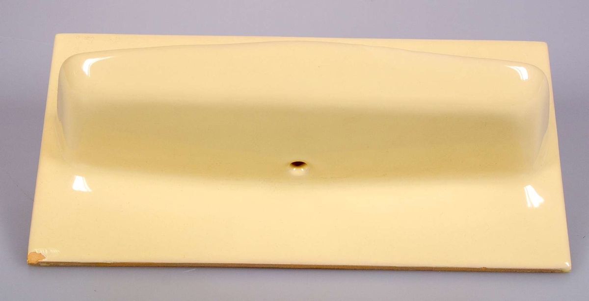 Kakelplatta med tvålkopp, gulglaserat tunt kakel, två kakelsbredd, av gulbrännande lera. På baksidan nedsänkt rand. Stämplad UE SWEDEN 710.