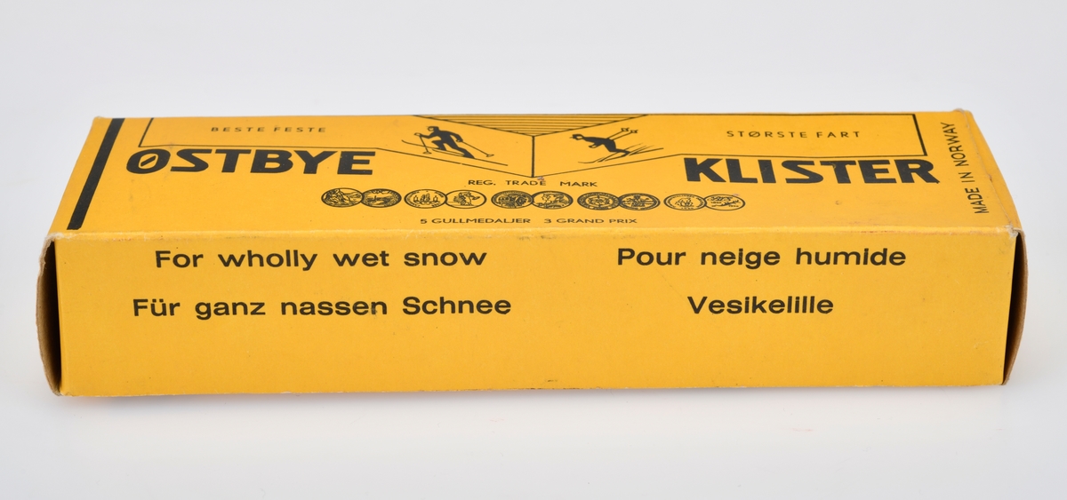 En eske med en tube med skiklister av typen Østbye Klister. Esken er av papp og er gul med svart tekst og dekor. For tekst se "Påført tekst/merker". På forsiden er det tegning av to skiløpere - en i motbakke og en i utforbakke. Det er også tegninger av medlajer/utmerkelser klisteret har vunnet. På baksiden er det en tegning som viser hvordan man skal påføre klisteret. Esken kan åpnes i begge kortendene. Tuben er av metall og korken er av svart plast. Tuben er gul med svart skrift/dekor. På forsiden er det tegning av to skiløpere - en i motbakke og en i utforbakke samt medaljer/utmerkelser klisteret har vunnet. På baksiden står det "For helt våt sne" på 10 ulike språk. I esken er det også en trespatel til å påføre klisteret med. Den er terhvit og laget av ubehandlet tre.