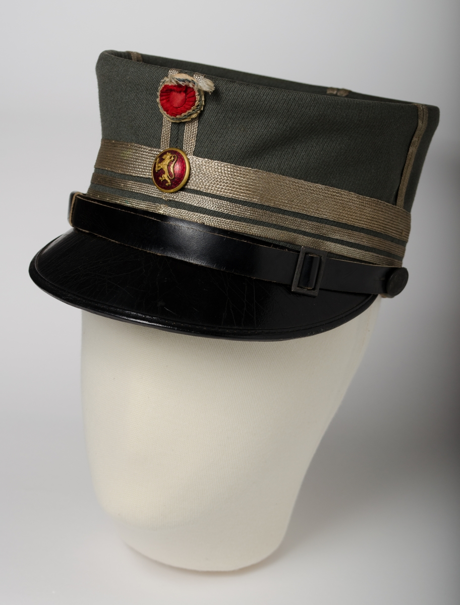 Jakke i grønn ull med syv metallknapper i front. Fire utenpåsydde lommer med klaff som lukkes med metallknapper.  Liten krave med flaskegrønn kanting, påsydd vinkel i sølvbånd og to stjerner. Kraven lukkes med to hekter. Innsiden har tre små nagler til løskrave. Ermene har spissformet mansjett, kantet med flaskegrønt bånd. Splitten bak, med legg på hver side avsluttes med metallknapp. Koksgrå, antagelig syntetisk fôr, ermene har lyst stripete bomullsfôr. Hemper i ermene. Innerlomme på venstre side; på denne er det festet et rensemerke. 

Bukse i grønn ulltekstil med bånd i sidene, flaskegrønne med grå stripe. Stikklommer og en baklomme. Gylf lukkes med fem plastknapper.Linningen lukkes med hempe i metall.  Seks plastknapper på yttersiden av linningen. Rensemerke på linningen. Bomullsfôr i linning. Beige lommefor. Splitt i linningen midt bak. 

Oval, grønn hatt med sort brem. Hatten er besatt med metallbånd, Bremmen er avsluttet med lærrem med to knapper og spenne. To knapper midt foran, en med den norske løve og en med rød, hvit og blå tøykanting. Fôret med rødt bomullsfôr og svettekant i lær.