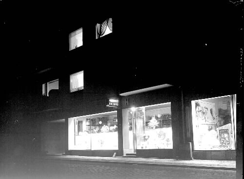 Varuhus. Skyltfönster upplysta på kvällen i varuhuset Halland. Torggatan 24, kv Sadelmakaren, Varberg. Beställare: Henning Rymander, innehavaren.