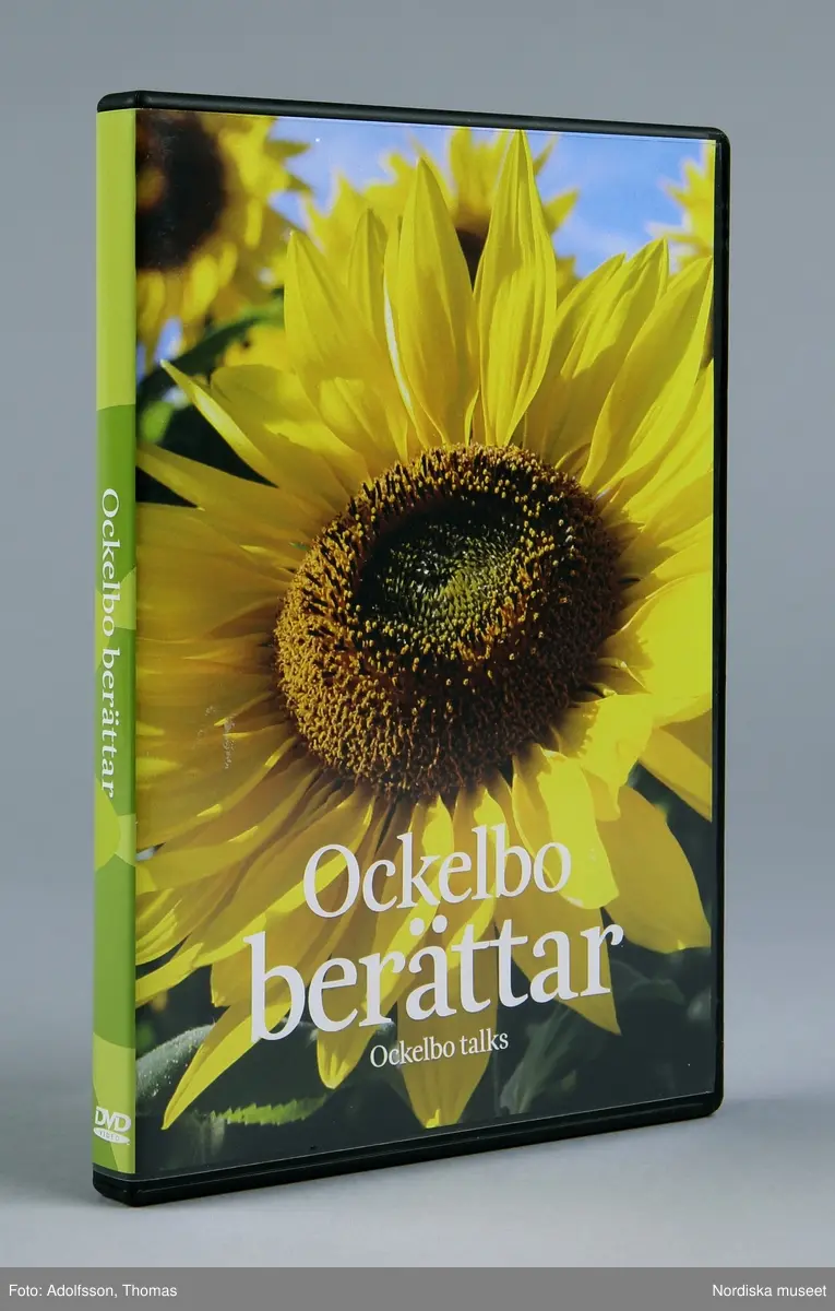 Fodral till DVD-skiva. Rektangulär "bok" av svart plast. På utsidan transparent plastficka innehålalnde tryckt papper med bild på solrosor på framsidan och text "Ockelbo berättar / Ockelbo talks" och på baksidan förklarande text om innehållet. Öppningsbar såsom en bok. inuti plats för en DVD-skiva med fastsättningsanordning (man trycker på mittknappen för att frigöra skivan) och två klämmor för broschyr.

Texten på baksidan
"Om att leva, bo och bedriva verksamhet i det riksbekanta Ockelbo berättar några människor från orten. Finns det en särskild anda i Ockelbo? Är klimatet särskilt gynnsamt här när företag ska etalberas, boplatser ska byggas eller när drömmar ska bli verklighet? Hur ser man egentligen på sin hembygd?
Ungdomar, pensionärer, nyinflyttade, etrepenörer och kreatörer ger alla sina bilder av livet på den lilla orten. Den lilla orten ed sina styrkor såväl som sina svagheter. Och ändå är det entsiasmen som lyser igenom när tron på möjligheter med råge överträffar problem och svårigheter.
Kanske är det så enkelt som att man inte har något vall när alternativet enligt kommularådet alrdig kan vara att slå sig till ro. Ett ständigt sökande efter nya lösningar och vägar, konventionella som okonventionella är det enda sättet att möta framtiden. Den som inte växer, den vissnar.
(samma text även på engelska)
En film av Dieter Stöpfgeshoff, speltid 22 min."
/Leif Wallin 2015-01-08