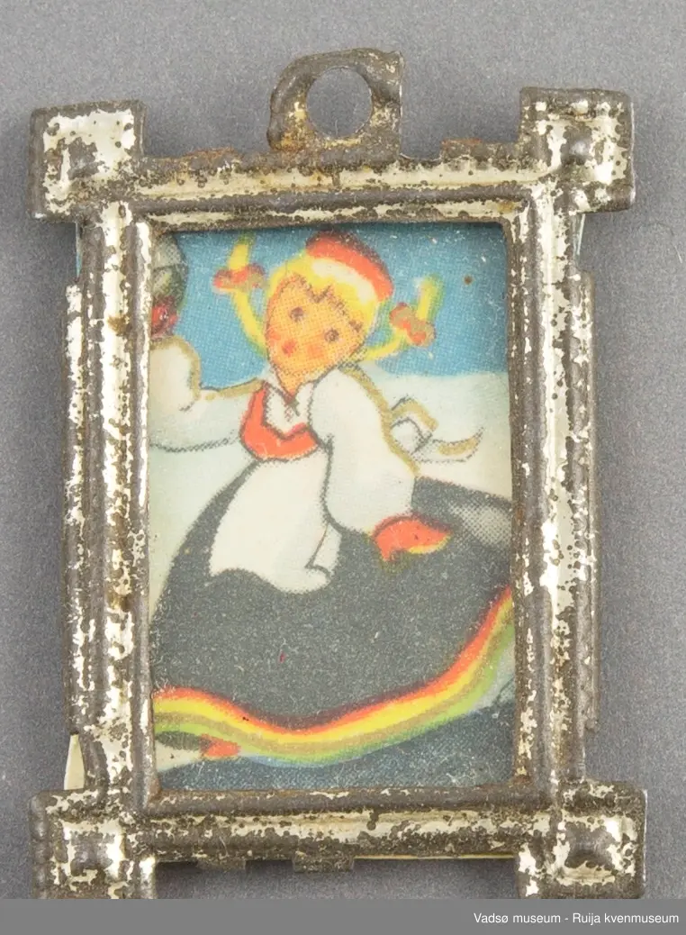 Dukkehusinventar. Bilde med glass og ramme. Rektangulær ramme i sølvfarget tynt metall, utformet i art deco stil. Kvadratisk vulst/ornament i hvert hjørne, øre med rundt opphengshull midt på ene kortsiden. Glasset er festet fast i rammen på baksiden.