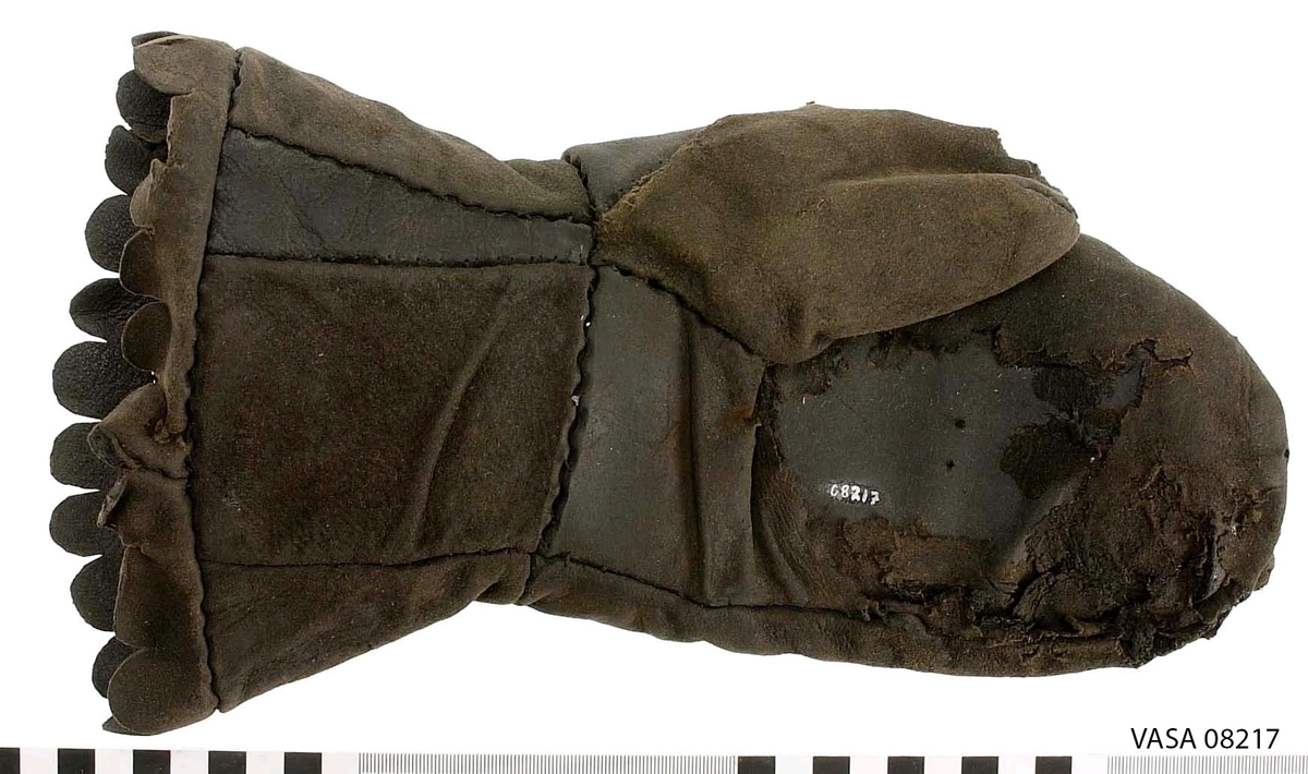 En kragvante till vänster hand. Sydd av flera kraftiga läderstycken. Påsydd bård i ett stycke i form av rundade "tungor" längs kragkanten.