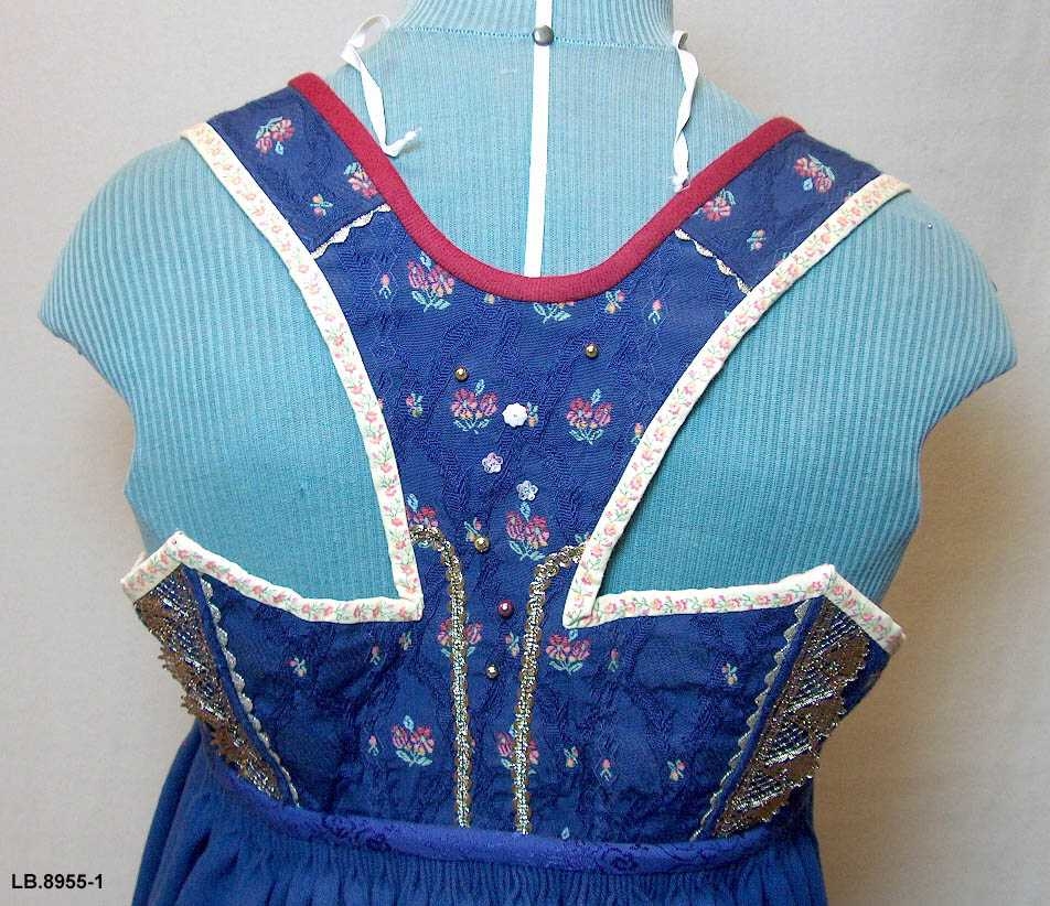 Uppluten sydd av blomstrete tøy og med perler bak. Kanta med ull og bomull. Pynta med agramaner i gull og sylv. Band til pynt, ingen broderi. 