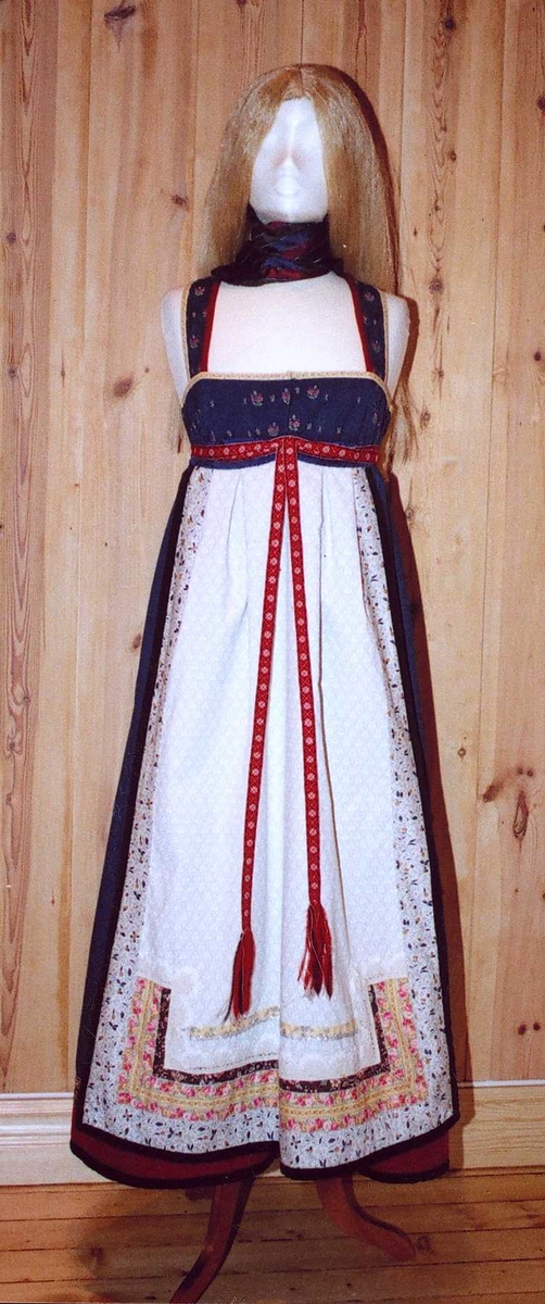 Uppluten sydd av blomstrete tøy og har perler bak. Kanta med ull og bomull. Bringekluten kan brukast på begge sider, raud på den eine, blå og lys gul på den andre. Forkleet kan og brukast på begge sider, blått på eine sida, lyst på den andre. Beltet skal brettast ned, slik at det framleis viser rettsida ut, når forkleet blir bruka på den blå sida. Forkleet er kanta med blått fløyelsband. Forkle, stakk og bringeklut er pynta med agramaner i gull og sylv. Band til pynt, ingen broderi. Drakta kan brukast i ulike samanhengar. Høgtidskledd med raud bringeklut. Med kvitt forkle er det eit endå meir høgtidsprega. Dersom ein i tillegg har la og belteklutar så er det brurestakk. Brukar ein lærbelte, er det meir kvardagplagg. Drakta kan varierast med forskjellige skjorter, sylv, plagg, og kan passe til mange typar bruk. Med den lyse sida av bringekluten fram er det meir kjøkkenfargr og meir sommarleg. Utan bringeklut kan ein bruke silkeplagg i bringa. Med  mindre pynt vert han tøffare, ein kan nesten bruke T-skjorte i staden for bunadsskjorte. 