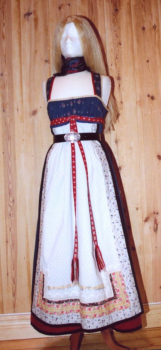 Uppluten sydd av blomstrete tøy og har perler bak. Kanta med ull og bomull. Bringekluten kan brukast på begge sider, raud på den eine, blå og lys gul på den andre. Forkleet kan og brukast på begge sider, blått på eine sida, lyst på den andre. Beltet skal brettast ned, slik at det framleis viser rettsida ut, når forkleet blir bruka på den blå sida. Forkleet er kanta med blått fløyelsband. Forkle, stakk og bringeklut er pynta med agramaner i gull og sylv. Band til pynt, ingen broderi. Drakta kan brukast i ulike samanhengar. Høgtidskledd med raud bringeklut. Med kvitt forkle er det eit endå meir høgtidsprega. Dersom ein i tillegg har la og belteklutar så er det brurestakk. Brukar ein lærbelte, er det meir kvardagplagg. Drakta kan varierast med forskjellige skjorter, sylv, plagg, og kan passe til mange typar bruk. Med den lyse sida av bringekluten fram er det meir kjøkkenfargr og meir sommarleg. Utan bringeklut kan ein bruke silkeplagg i bringa. Med  mindre pynt vert han tøffare, ein kan nesten bruke T-skjorte i staden for bunadsskjorte. 