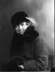 Porträtt av ung kvinna i vinterkappa och hatt med fjäder. Det är möjligen Mimmi Allard.