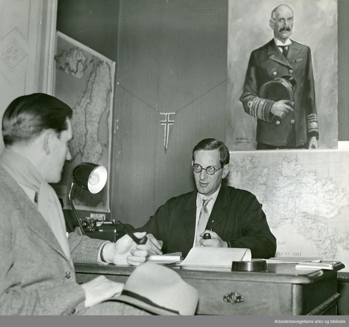 NORWEGIAN OFFICIAL PHOTO NO. S 5464. Bildet er hentet fra informasjonskontoret på Kjesäter. En nyankommen flyktning intervjues av redaktør Einar Foss. Portrett av Kong Haakon 7. Stockholm 1.2.1945. Se også Andre opplysninger..