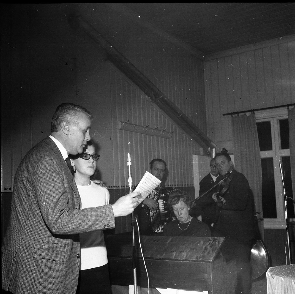 Bertil Perrolf och en kvinna sjunger, kompad av kvinna på piano samt tre män på dragspel, fiol och kontrabas.