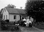 Familj sittandes i trädgården framför bostadshuset.
Morföräldrar till Gösta Ivarsson.
Juli 1913.