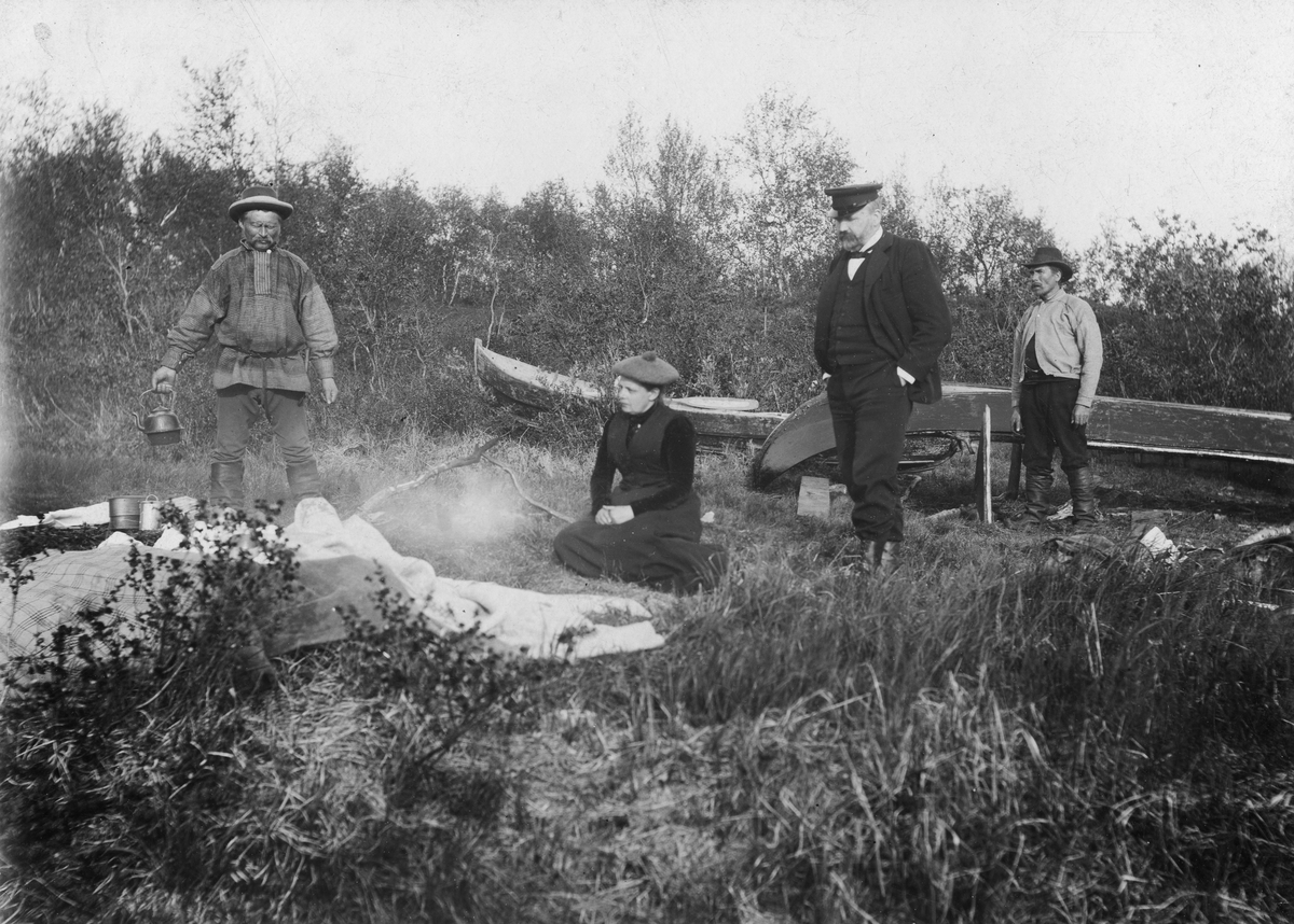 Ekteparet Wessel på utflukt. Sittende midt i bildet Ellisif Wessel, stortingsmann Håkon Finstad står ved siden av henne. To ukjente menn er også med, til venstre sannsynligvis vappusen - kjentmannen holder på å koke kaffe. Ukjent sted, sannsynligvis langs Pasvikelva ca år 1900.