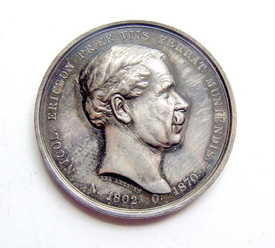 Minnesmynt av silver med profil av Nils Ericson på ena sidan och latinsk text: "Nicol. Ericson Praef. Viis Ferrat. Muniendis N. 1802 O. 1870". (Nils Ericson, chef för järnvägsbyggnaderna född 1802 död 1870).
På andra sidan syns Merkurius som fäster sina vingar på fötterna, samt texten: "Cursu veloci ut iungat disiuncta" (För att med snabbt lopp förena åtskilda platser). Under Merkurius står texten:
"Socio Meritissimo / canal et viar ferr artifici / r ac scient suec / MDCCCLXXXV (Kungliga Svenska Vetenskapsakademien för sin synnerligen förtjänte ledamot, konstruktionen av kanaler och järnvägar år 1885).
