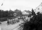 Regementsgatan, 1920-talet

Vid hemmarsch från övningar mötte ofta musikkåren. Här går marschen på Regementsgatan i höjd med seminariet på den stora tomten t.v. (senare Thomasgymnasiet och badhuset)

Kåren leds av regementstrumslagare Nygren, som tog avsked 1928.
Bakom musikkåren rider fyra officerare, den kraftige i uniform m/Ä är kapten Nordenskjöld.