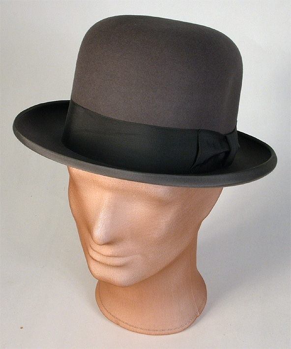 Herrhatt av grå filt med grått ripsband runt kullen. Rosa foder. 
   Mått: Runt kullen 560 mm. Kullens höjd 140 mm. 
   Storlek: 58.