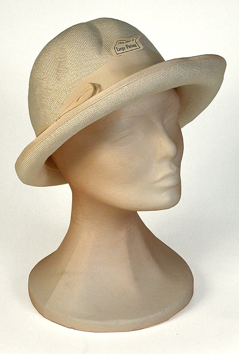 Damhatt av vitt viskos, rund formpressad kulle, rosett i höger sida. 
   Mått: Runt kullen 590 mm. Kullens höjd 130 mm.