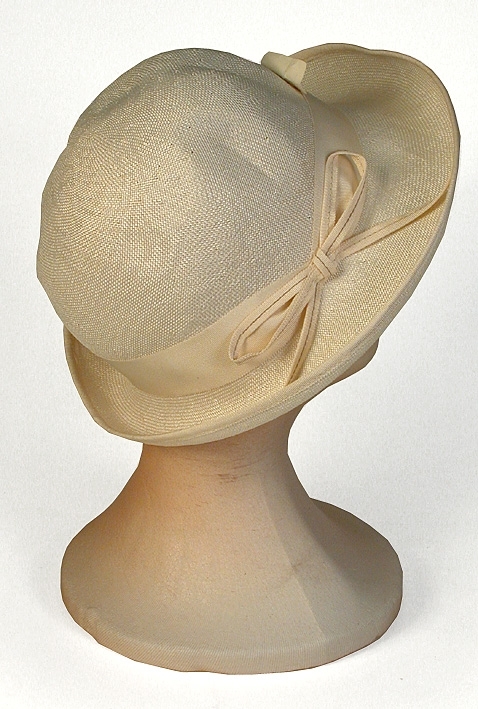 Damhatt av vitt viskos, rund formpressad kulle, rosett i höger sida. 
   Mått: Runt kullen 590 mm. Kullens höjd 130 mm.