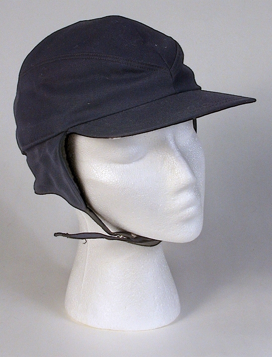 Herrmössa, skärmmössa (sport). Kilskuren kulle. Uppvikt vid sidorna. 
   Mått: Runt kullen 490 mm. Kullens höjd 170 mm. 
   Storlek: 55.