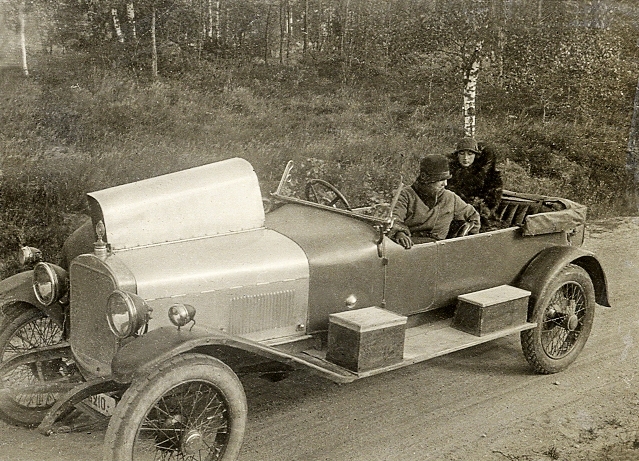 En bil, en Sunbeam med registreringsnummer G 210, som stannat vid en vägren, p g a motorkrångel. Chauffören skymtar bakom motorhuven. I bilen sitter två kvinnor och väntar. Bilen deltog i flertalet lokala tävlingar, framförd av paret grosshandlare Markus och Karen Markussen, Alvesta. Möjligen är det paret Markussen som syns på bilden.