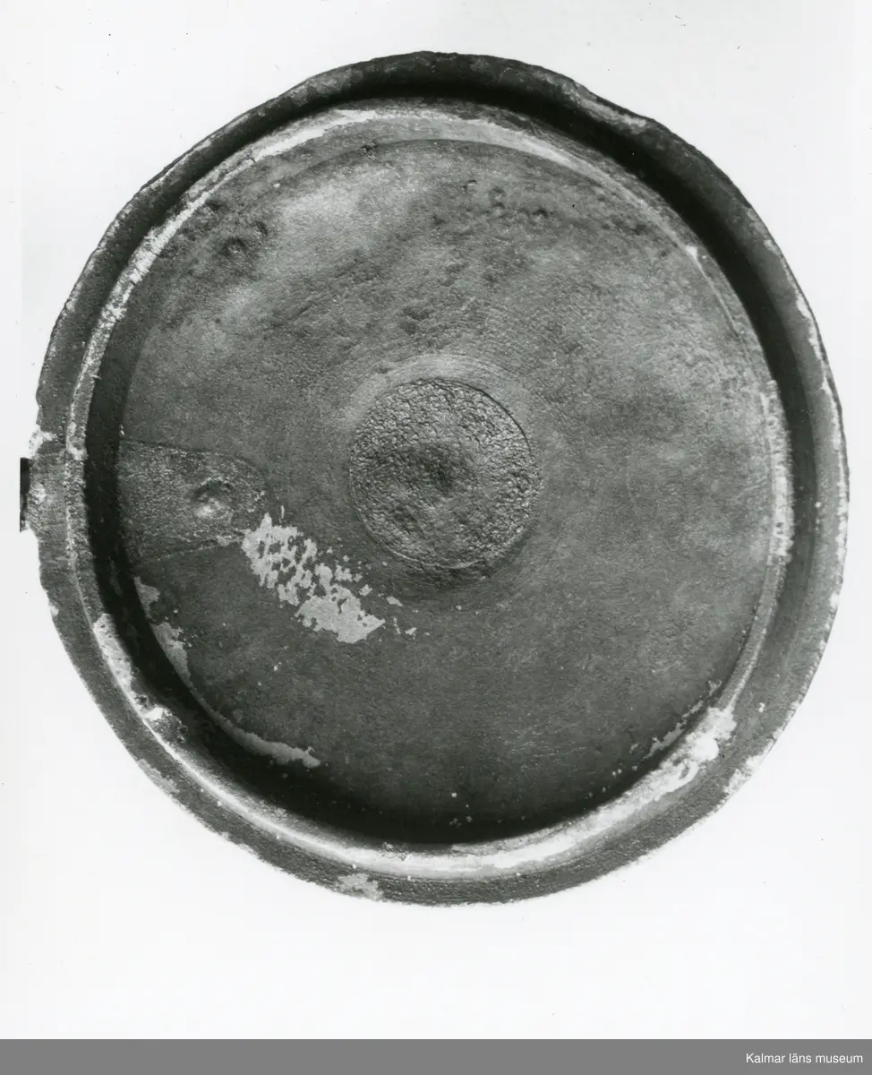 KLM 46428 Kanna av tenn. Bukig form. Hankkärl, försedd med lock och handtag, vidgad botten neråt. I botten, invändigt en medalj med korsfästelsebild. Medaljens kant försedd med pärlring. Ägarmärke/bomärke på lockets och bottens utsidor. Handtaget ornerat med drakmotiv och bladslinga, tumgreppet saknar ett av ekollonen. Kannan skadades svårt vid upphittandet, genomgående sprickor på många ställen.