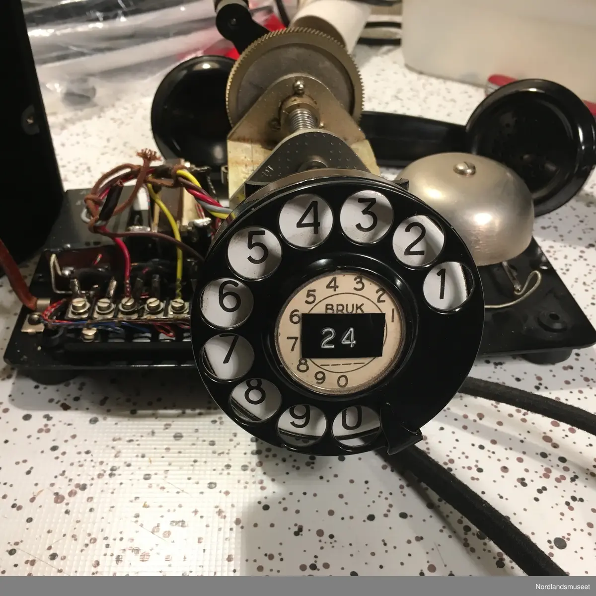 Telefonapparat med sveiv og nummerskive
Kombimodell, som kan benyttes i manuelt og automatisk telefonnett.
Bunnplate merket med AD 51775
Merkelapp på ledning merket med: "2. nov 1951" og "MEURICE BRUXELLES"
Produsent er noe usikker.