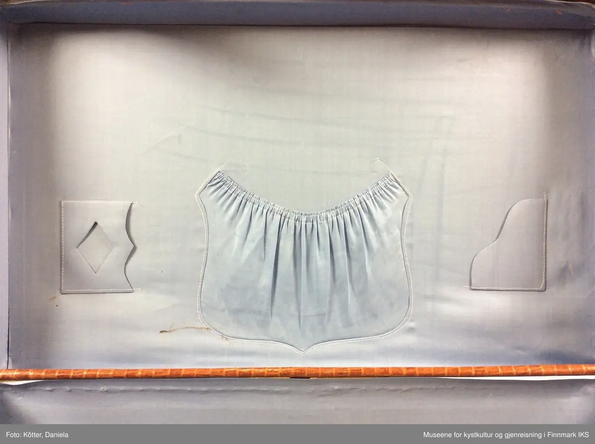 Reisekofferten er laget av kryssfinér og er overtrukket med skinnimiterende materiale av plast. Innvendig er den utkledd med lyseblå stoff. I lokket er det sydd inn tre forskjellige lommer. Kofferten inneholder noen avissider. Kofferten bærer merker etter reisene den ble brukt til, et pappetikett fra Wilhelmsen Lines  og en klistremerke fra NSB.