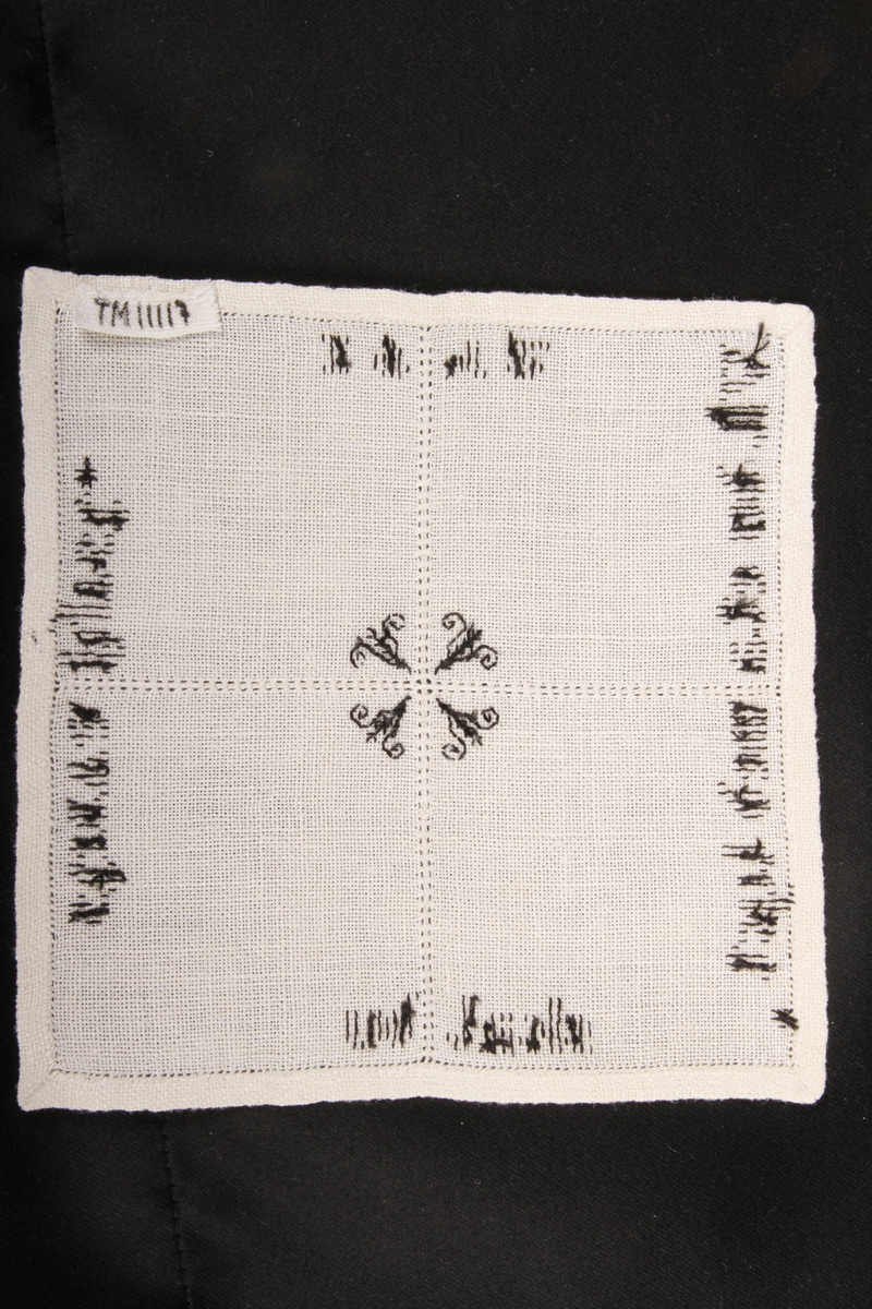 Vevd, naturfarge med svart dekor, brodert korsting, hullsøm, attersting. Border, tekst og blomster.