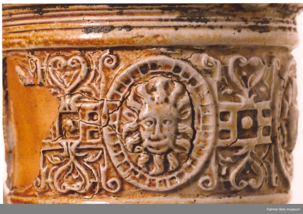 KLM 1712. Krus av stengods. Saltglaserat. Bukigt. Krus med hänkel. Lock och fot av tenn. Tumgrepp: klogrepp. Rhenkrus med bandinskription och årtalet 1583. Inskription: Geret du mus daper blasen, so dansen die buren, als waren se rasen, fri uf, spricht pastor, ich ver dans, di kap mit den kor. Reliefmodelerad dekor. Keramik av Siegburgtyp, Tyskland.