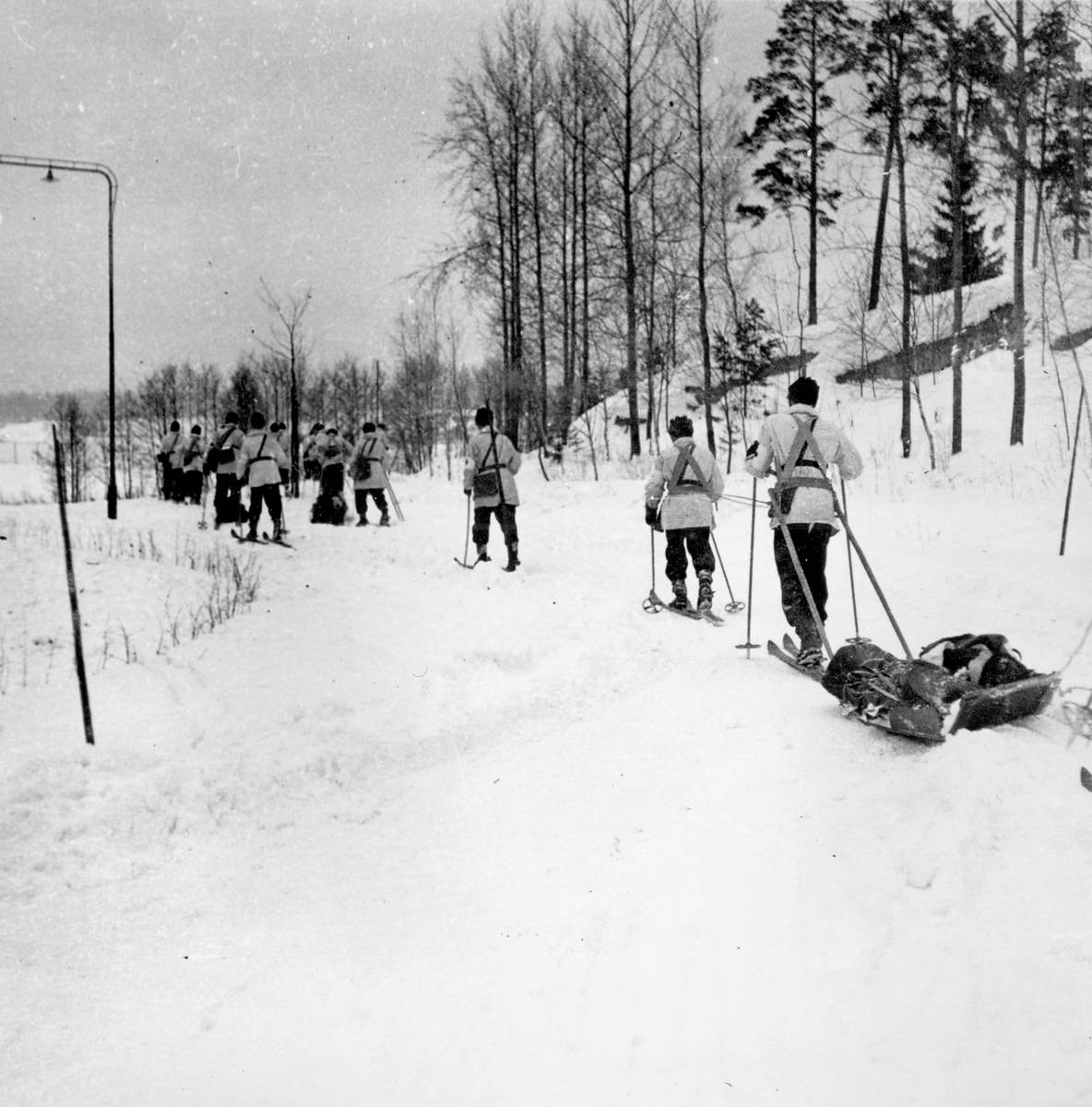 Skidåkande soldater i vinteruniform på väg mot sjukvårdsövning i fält vid F 11 Södermanlands flygflottilj, 1945.

Vintertid.

Ur fotoalbum "Sjukvårdsskolan 15/1-15/3 1945" från F 11.