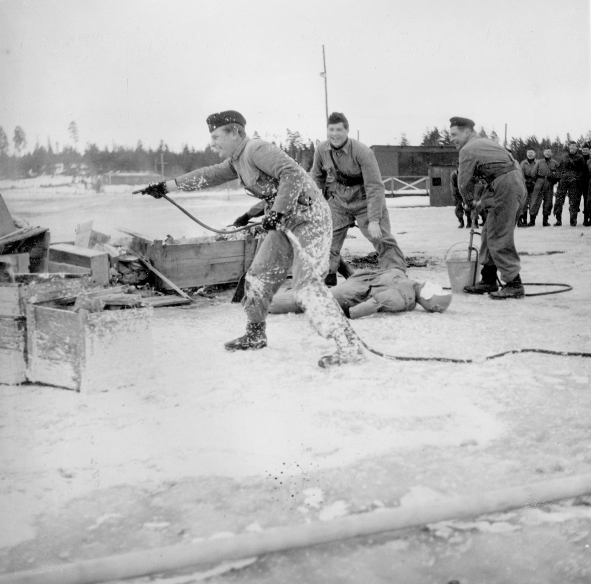 Soldater övar brandsläckning av flygplansattrapp med brandskum vid sjukvårdsövning på F 11 Södermanlands flygflottilj, 1945.

Vintertid.

Ur fotoalbum "Sjukvårdsskolan 15/1-15/3 1945" från F 11.