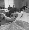 Mätning av blodtryck under sjukvårdskurs på F 11 Södermanlands flygflottilj, 1945. En man i en sjuksäng i skolsal. Elever i skolbänkar i bakgrunden.

Ur fotoalbum 