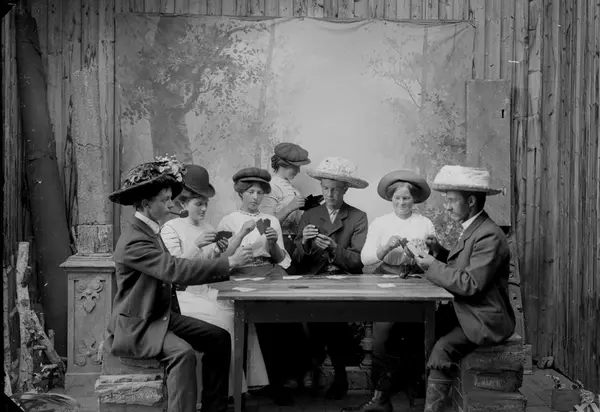 Studioportrett, gruppe. Menn og kvinner sittende ved spilleb