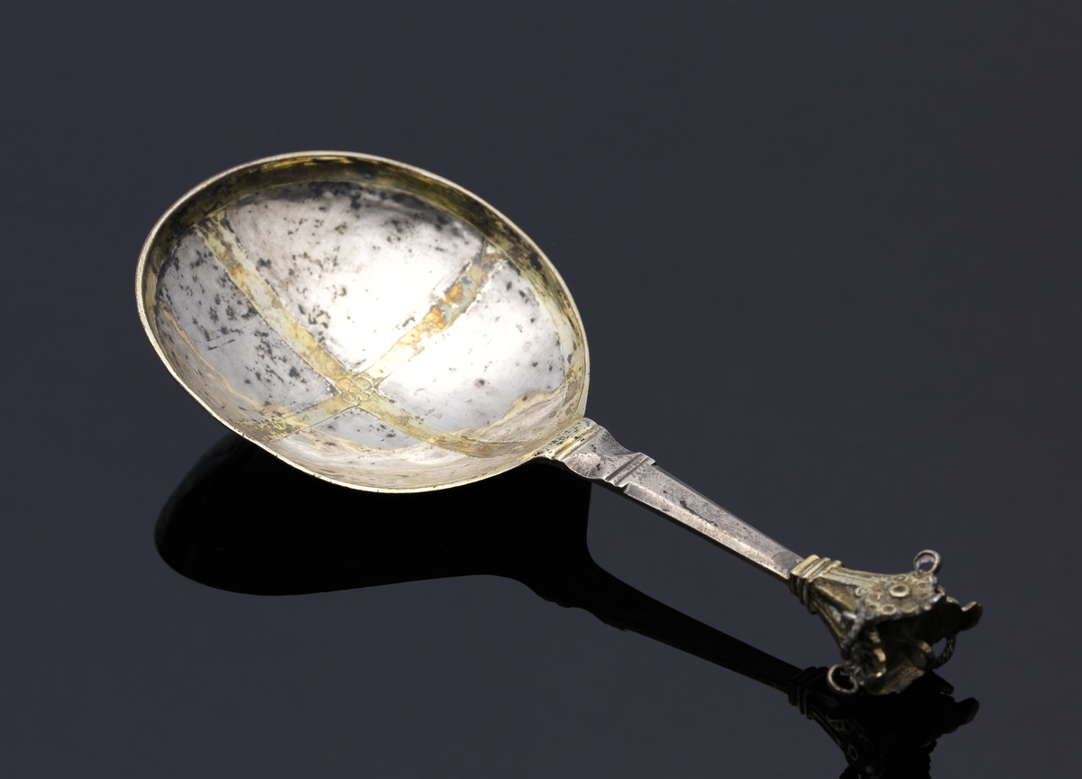 Brännvinssked av silver. 
S.k. kronsked med nästan runt skedblad, kort platt skaft, dekorerat med tvärräfflor längst ner. Skaftknopp i form av krona, 
sammansatt av fyra gotiska korsblommor. I kronans hörn hänger spiralvridna ringar (två saknas). 
Bladet har dekor i form av ett förgyllt kors med en graverad blomma i mitten. Även inre kanten av bladet är förgyllt. 
Stämplar och s.k. åldermansranka på skaftets baksida.

Inskrivet i huvudbok 1867.