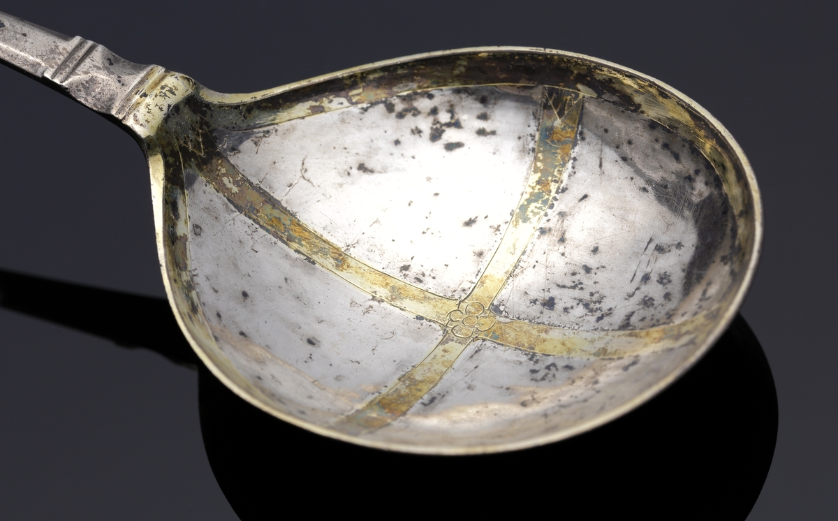 Brännvinssked av silver. 
S.k. kronsked med nästan runt skedblad, kort platt skaft, dekorerat med tvärräfflor längst ner. Skaftknopp i form av krona, 
sammansatt av fyra gotiska korsblommor. I kronans hörn hänger spiralvridna ringar (två saknas). 
Bladet har dekor i form av ett förgyllt kors med en graverad blomma i mitten. Även inre kanten av bladet är förgyllt. 
Stämplar och s.k. åldermansranka på skaftets baksida.

Inskrivet i huvudbok 1867.