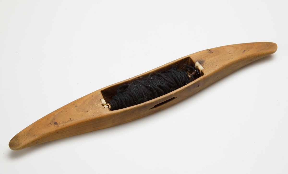 Vävskyttel av trä (8 st).
Vågformad kontur. Avlångt hål med små benplattor omkring hålen för stången. 
a) med svart tråd
f) med tom tråd "tuta". 1894 skrivet med bläck.
Resterande skyttlar är tomma.

Mått:
Längd: 280 mm
Längd hål: 90-105 mm
Bredd: 35-45 mm