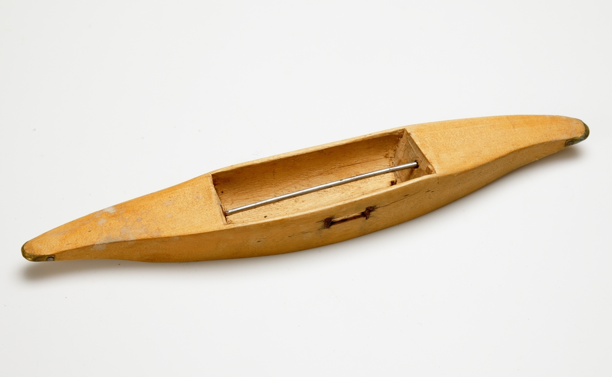 Vävskyttel av trä (8 st).
Vågformad kontur. Avlångt hål med små benplattor omkring hålen för stången. 
a) med svart tråd
f) med tom tråd "tuta". 1894 skrivet med bläck.
Resterande skyttlar är tomma.

Mått:
Längd: 280 mm
Längd hål: 90-105 mm
Bredd: 35-45 mm