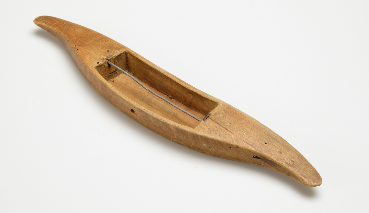 Vävskyttel av trä (8 st).
Vågformad kontur. Avlångt hål med små benplattor omkring hålen för stången. 
a) med svart tråd
f) med tom tråd "tuta". 1894 skrivet med bläck.
Resterande skyttlar är tomma.

Mått:
Längd: 280 mm
Längd hål: 90-105 mm
Bredd: 35-45 mm