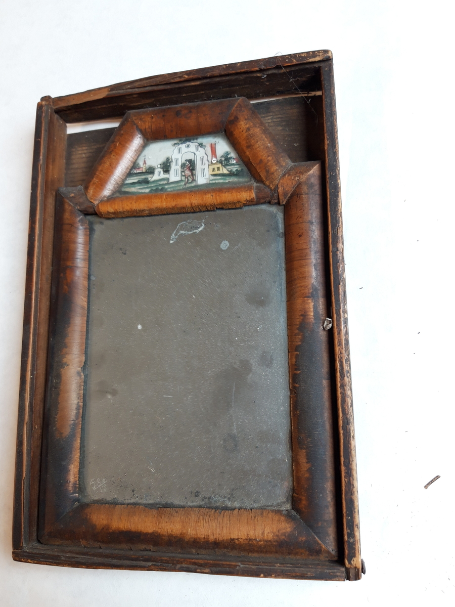 Speilet er laget av ei fururamme som er finért. Det er innfelt et lite maleri som er malt på baksiden av glass. Speilet er et amalgamspeil. mellom speil og bakplate lå et håndskrevet ark. 