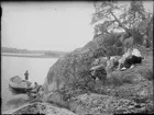 Josef Edhlund sitter på klipporna tillsammans med en man och två kvinnor. Två barn är vid en båt , Östhammar, Uppland